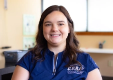 Dr Abby Smiling chiropractor in CORE Health Centers uniform, seated in a treatment room, representing Dr. Kaysie Adair, D.C.