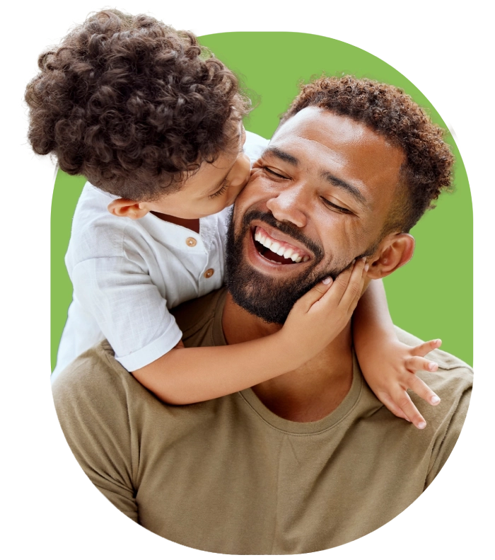 manandson (1) A young child with curly hair kisses a smiling man with a beard on the cheek. The man, who looks like he could be a friendly chiropractor from a health center, is holding the child, and both display happiness. The background is a plain green circle.